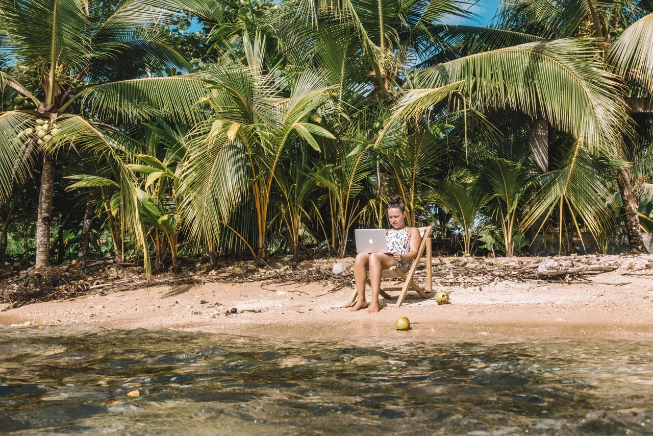 a woman is working on a laptop at the beach