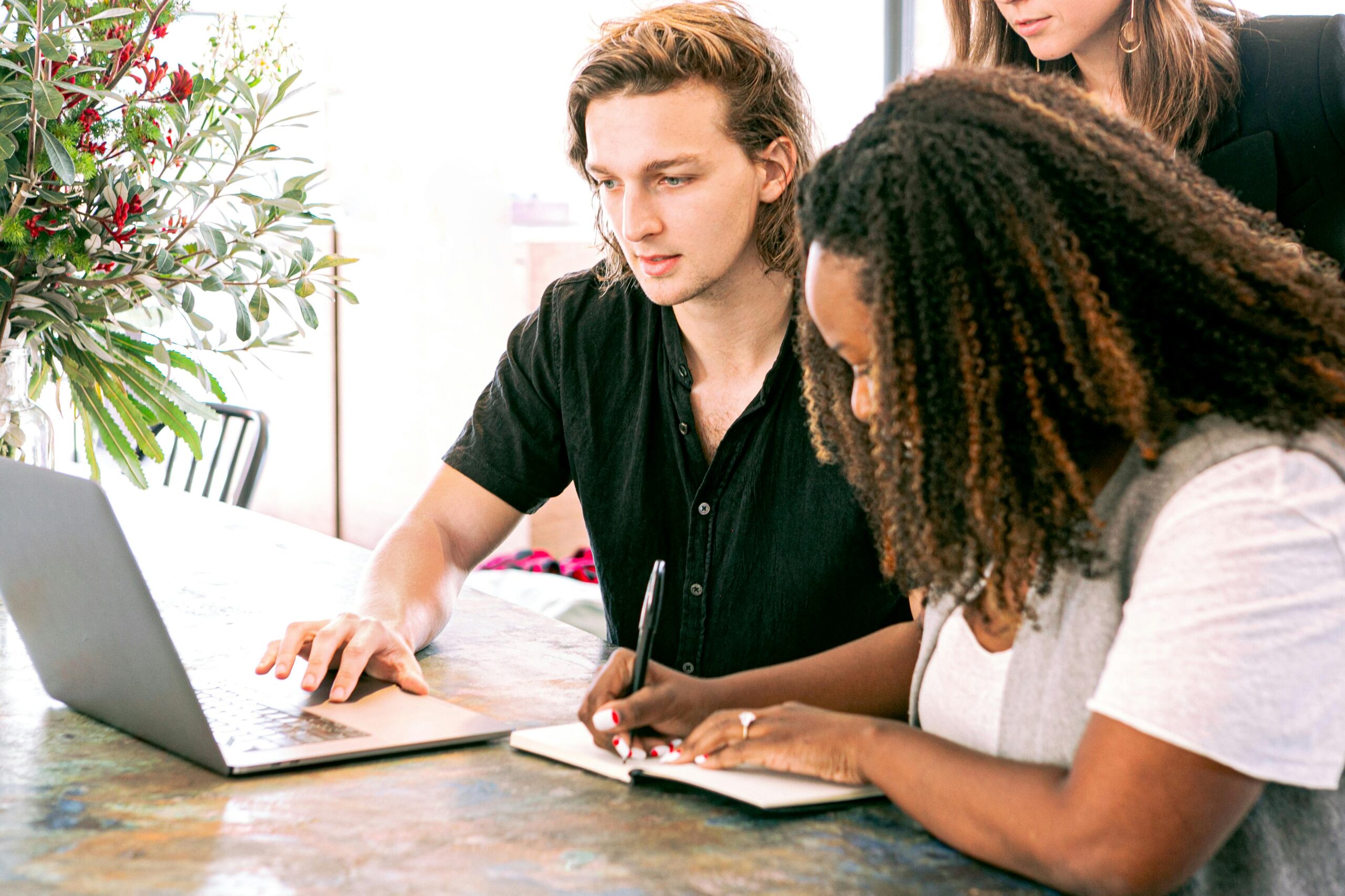 Man and woman working together, writing notes and using a laptop